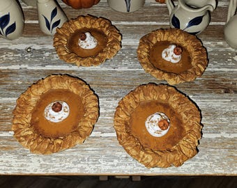 May include: Four miniature pumpkin pies with whipped cream and a decorative pumpkin on top. The pies have a golden-brown crust and a rich, orange filling. They are arranged on a weathered, light-colored wooden surface, suggesting a rustic theme.