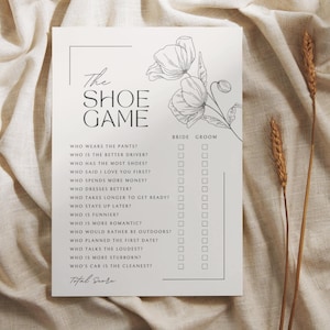 May include: A white card featuring "The Shoe Game" text and a floral design. The game includes questions such as "Who wears the pants?" and "Who is the better driver?" with Bride and Groom answer spaces.