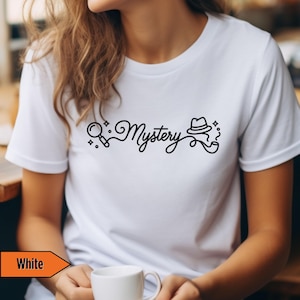 May include: White t-shirt with a black graphic that reads "Mystery" in a cursive font, accompanied by a magnifying glass, a hat, and a pipe. The shirt is plain and has short sleeves.