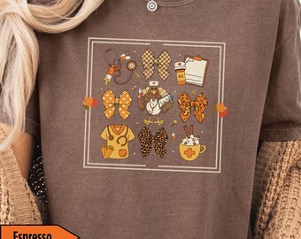 May include: Espresso-colored t-shirt featuring a square design with fall-themed medical and Thanksgiving graphics. The design includes bows, a stethoscope, a turkey, and a coffee cup. The shirt is a crew neck style.