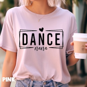 May include: A light pink t-shirt with the words "DANCE nana" in a black rectangular frame. A small black heart is above the word "DANCE". The word "PINK" is printed in the lower left corner of the shirt.