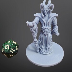 Puede incluir: Una figura miniatura de plástico gris de un demonio con cuernos y un bastón. La figura está de pie sobre una base redonda. Un dado de 13 caras verde y blanco está en primer plano.