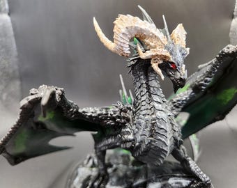 Può includere: Statuetta dettagliata di un drago con squame nere, ali tinte di verde e corna color cuoio. Il drago ha occhi rossi ed è posizionato con le ali spiegate. La scultura è su una base grigia.