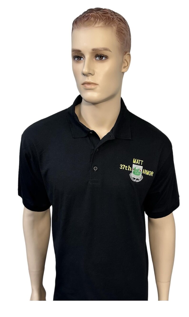 May include: A black short-sleeved polo shirt with a collar and a three-button placket. Embroidered on the left chest in yellow and green thread is the text MATT 37th ARMOR above a shield-shaped emblem featuring a green dragon graphic.