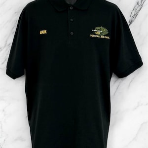 May include: A black short-sleeved polo shirt with a collar and three buttons. The right chest features the name MARK in yellow embroidery. The left chest displays an embroidered green tank with the text M88 YOU CALL WE HAUL in yellow.