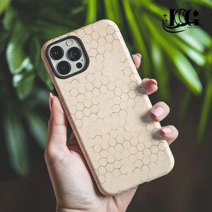 May include: A blush-colored phone case with a gold honeycomb pattern. The case has a black camera ring and is held in a hand. The logo "ICG COMPANY" is in the upper right corner.