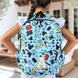May include: A light blue backpack with a Mickey Mouse print. The backpack has a large letter "A" on the front. The backpack is decorated with Mickey Mouse ears, hands, and stars.
