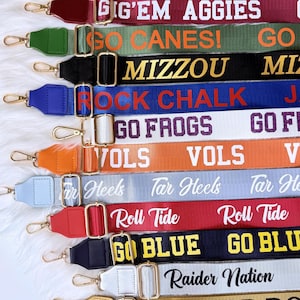 Puede incluir: Una colección de correas de bolso coloridas y estampadas con herrajes dorados. Cada correa presenta un nombre de equipo o frase diferente, incluyendo "GAME DAY", "GIG'EM AGGIES" y "GO BLUE". Las correas se muestran sobre una superficie blanca y esponjosa.