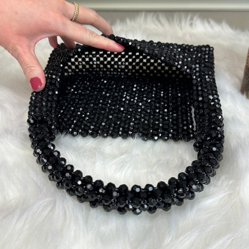 May include: A black beaded handbag with a woven design. The bag has a top handle and is made of small, round beads.