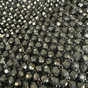 May include: Close-up of a black beaded fabric with a textured, diamond-shaped pattern. The beads are small and tightly woven together.