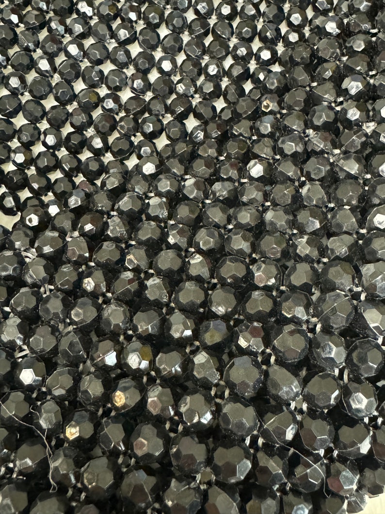 May include: Close-up of a black beaded fabric with a textured, diamond-shaped pattern. The beads are small and tightly woven together.