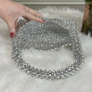 May include: A silver beaded handbag with a round, open top. The bag is made of small, round beads that are woven together.