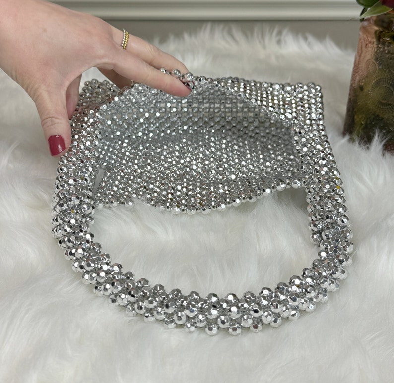 May include: A silver beaded handbag with a round, open top. The bag is made of small, round beads that are woven together.