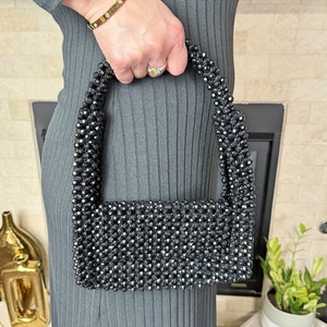 May include: A black beaded handbag with a rectangular shape and a short strap. The bag is made of small, black beads that are woven together.