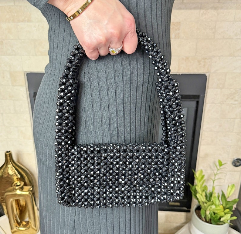 May include: A black beaded handbag with a rectangular shape and a short strap. The bag is made of small, black beads that are woven together.