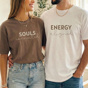 Può includere: Due persone indossano magliette abbinate. Una maglietta è marrone con la scritta "SOULS connected" in bianco. L'altra maglietta è bianca con la scritta "ENERGY aligned" in marrone. Entrambe le magliette sono a maniche corte.