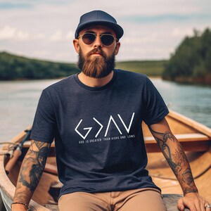 May include: A navy blue t-shirt with a white graphic of the words "God is greater than highs and lows" with an arrow pointing up between the words "God" and "is".
