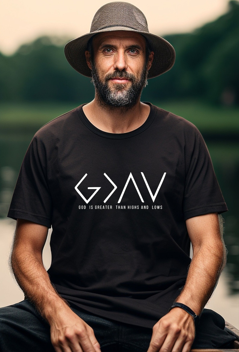 May include: A man wearing a black t-shirt with a white graphic that says "G>A>V" and "GOD IS GREATER THAN HIGHS AND LOWS". He is wearing a brown hat and has a beard.