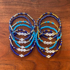 May include: A set of 10 friendship bracelets with blue, turquoise, and gold beads. The bracelets have the letters "FTP" and a heart charm.