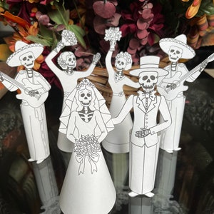 May include: A set of six paper cut-outs of skeletons dressed in wedding attire. The bride and groom are in the centre, with two musicians and two guests on either side. The skeletons are all wearing traditional Mexican wedding attire, including sombreros, suits, and dresses. The bride is holding a bouquet of flowers.