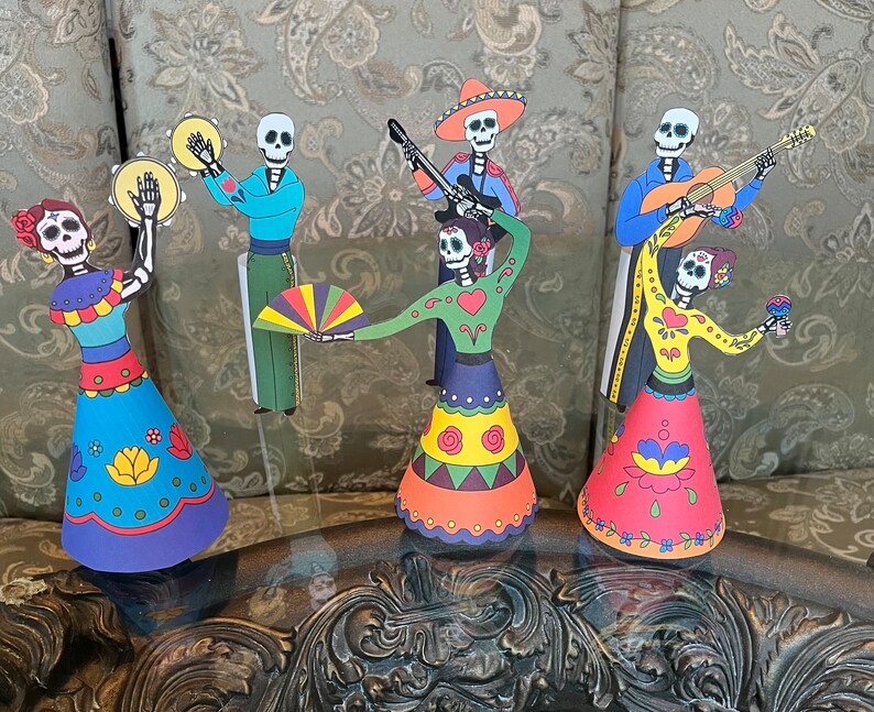 May include: A set of six Day of the Dead paper figures, each with a unique design and colorful clothing. The figures include a musician playing a guitar, a musician playing a tambourine, a dancer with a fan, and three dancers with flowers.
