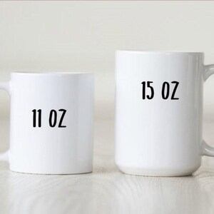 May include: Two white ceramic mugs. The smaller mug has "11 OZ" printed in black. The larger mug has "15 OZ" printed in black. Both mugs have a curved handle.