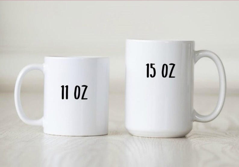 May include: Two white ceramic mugs. The smaller mug has "11 OZ" printed in black. The larger mug has "15 OZ" printed in black. Both mugs have a curved handle.