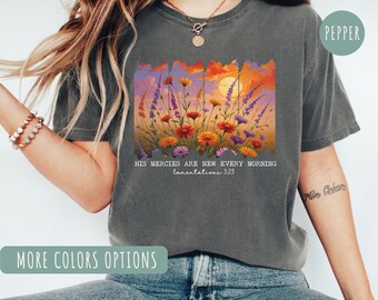 May include: Dark gray t-shirt featuring a colorful floral design with a sunset background. The text "HIS MERCIES ARE NEW EVERY MORNING Lamentations 3:23" is printed below the image. The shirt has short sleeves.
