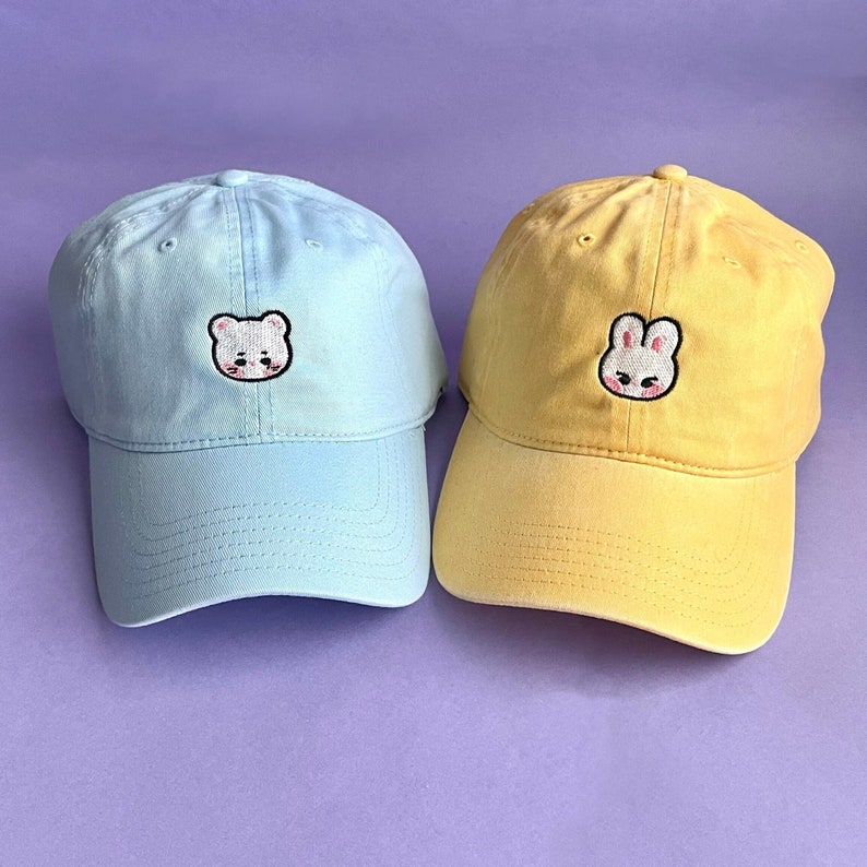 Left: Powder Blue dad cap with Jiniret (white ferret) Skzoo embroidered on the center. Right: Yellow dad hat with Leebit (white bunny) Skzoo embroidered on the center.