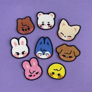 May include: Eight embroidered iron-on patches featuring various animal faces with different expressions. The patches are on a purple background. The animals include a bear, a cat, a bunny, a dog, a chick, and two other animals.