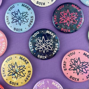 May include: A collection of round pinback buttons in various colors, including blue, pink, yellow, and purple. Each button features the words "STAY," "YOU," "MAKE," and "KIDS" around a central starburst design.