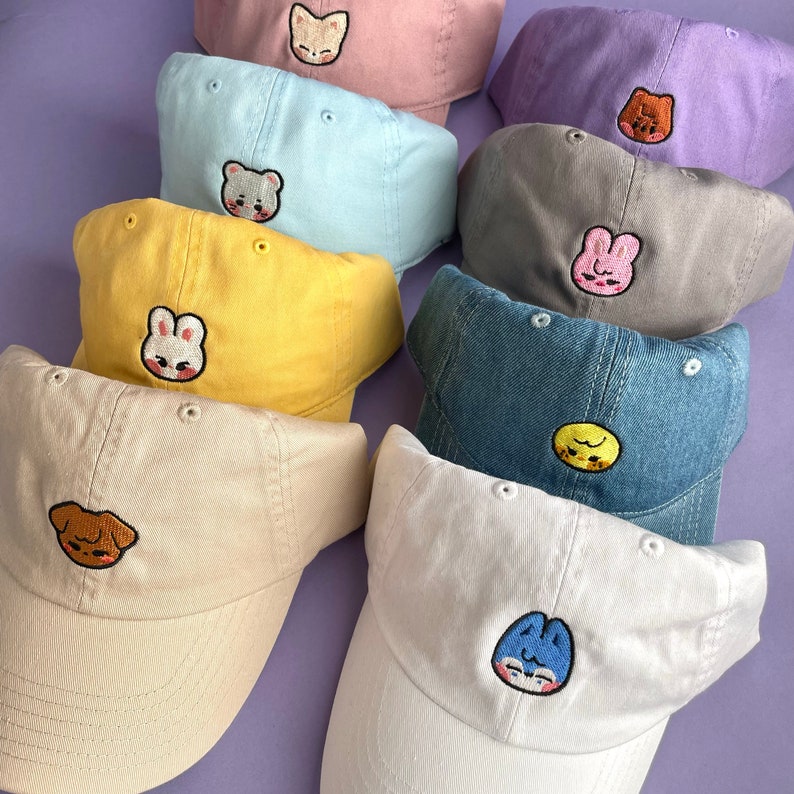 Pode incluir: Nove bon&eacute;s de beisebol bordados em v&aacute;rias cores com diferentes desenhos de animais. Os bon&eacute;s est&atilde;o dispostos em semic&iacute;rculo sobre um fundo roxo.