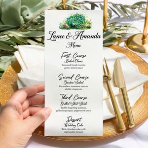 May include: A wedding menu with a peacock illustration. The menu lists the courses: Baked Clams, Garden Salad, Grilled Shirt Steak, and Wedding Cake.
