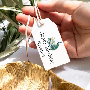 May include: White gift tag with a peacock design and the text "Happy Birthday Kristen".