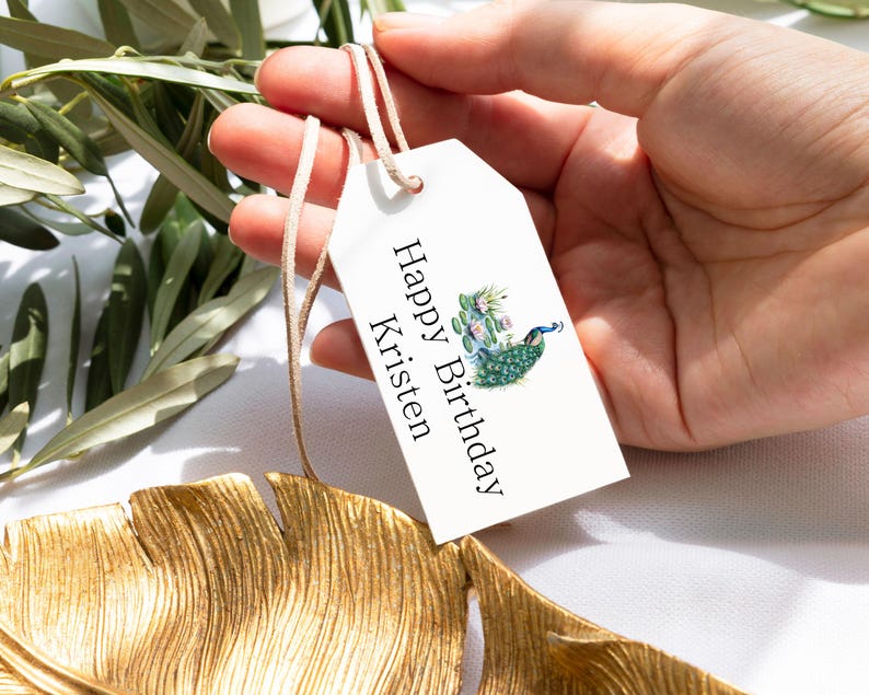 May include: White gift tag with a peacock design and the text "Happy Birthday Kristen".