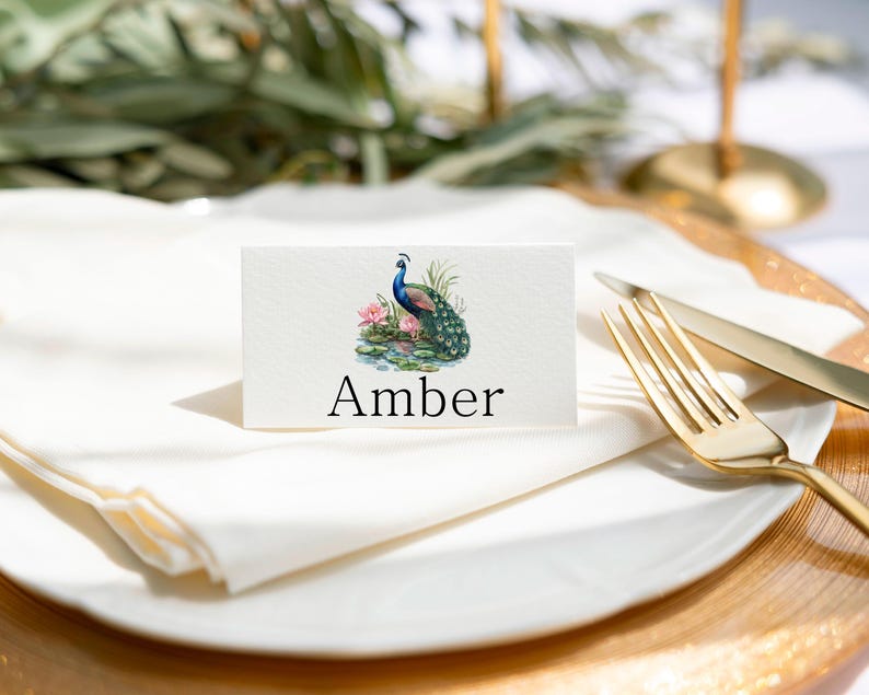 May include: A white place card with a peacock illustration and the name "Amber" printed in black.