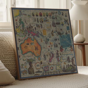 May include: A framed vintage map of Oceania, with detailed illustrations and a blue border. The map is displayed on a white surface, leaning against a pillow. The map includes illustrations of people, animals, and ships.