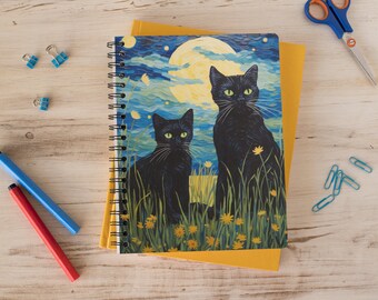 Op de afbeelding: Een spiraalgebonden notitieboek met een zwarte en blauwe omslag met twee zwarte katten die in een veld met gele bloemen onder een volle maan zitten.