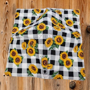 May include: A black and white checkered fabric with a pattern of yellow sunflowers. The fabric is folded in half and has a white seam around the edges.