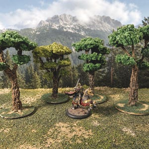 Op de afbeelding: Vier miniatuurmodelbomen met getextureerde bruine stammen en groen gebladerte, elk gemonteerd op een ronde voet. Tussen de bomen staat een miniatuurfiguur van een ridder in harnas op een paard, met rode en gouden details.