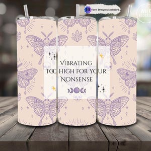 May include: A set of three insulated tumblers with a light beige background and a repeating pattern of purple moths, crystals, and celestial elements. The center tumbler features the text "Vibrating Too High For Your Nonsense."