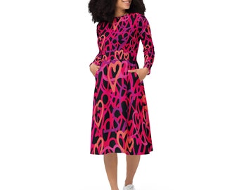 May include: A black midi dress with a pink and orange heart print. The dress has long sleeves and pockets.