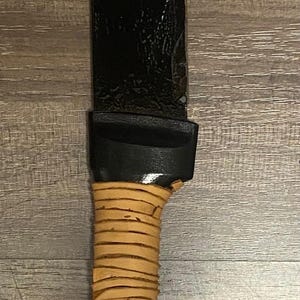 May include: A black curved blade with a brown leather wrapped handle.