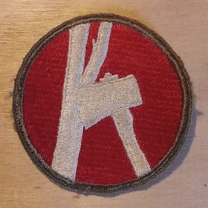 May include: A red and white embroidered patch with a white axe design. The patch is circular and has a brown border.