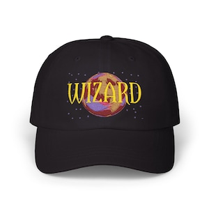 May include: Black baseball cap with the word "WIZARD" embroidered in yellow above a colorful planet design. The planet features shades of brown, purple, and gold. Small purple stars are embroidered around the planet.