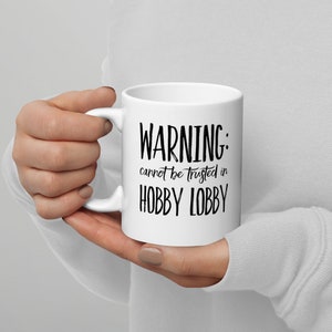 Puede incluir: Taza de cerámica blanca con texto negro que dice "WARNING: cannot be trusted in HOBBY LOBBY".