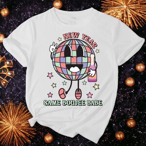 May include: White t-shirt with a colorful disco ball graphic holding a bottle of champagne. The text "New Year Same Boujee Babe" is printed below the graphic.