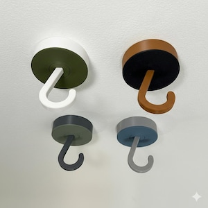 Op de afbeelding: Vier plafondhaken in verschillende kleuren: wit en olijfgroen, bruin en zwart, grijs en blauw. Elke haak heeft een cirkelvormige basis en een gebogen haak. De haken zijn ontworpen om items op te hangen.