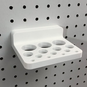 May include: White plastic pegboard organizer with multiple round holes of varying sizes. The organizer is designed to hold paint tubes or other small items.