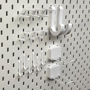 Pode incluir: Painel perfurado branco com vários ganchos e acessórios de prateleira brancos. Inclui vários suportes de prateleira pequenos, ganchos em forma de J e ganchos quadrados com braços de arame. O painel perfurado tem orifícios espaçados para organização versátil.